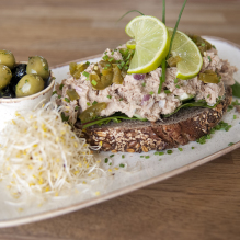 A plate with tuna salad sandwich with olives and alfalfa