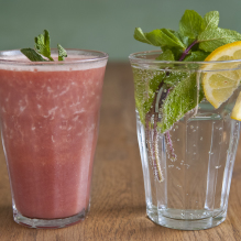 A glass with a red smoothie and one with sparkling water with mint and lemon