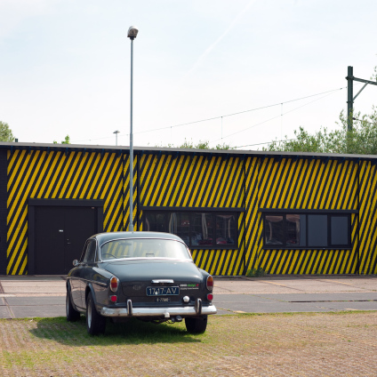 Exterior photo of an old timer car in front of a yellow and black striped wall