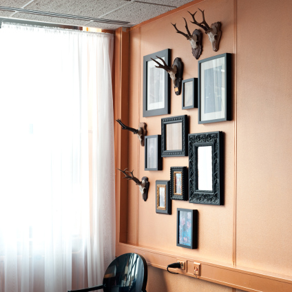 An interior photo of an orange wall with picture frames and antlers
