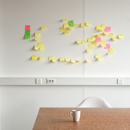 An interior photo of a table, cup and a wall with post-its